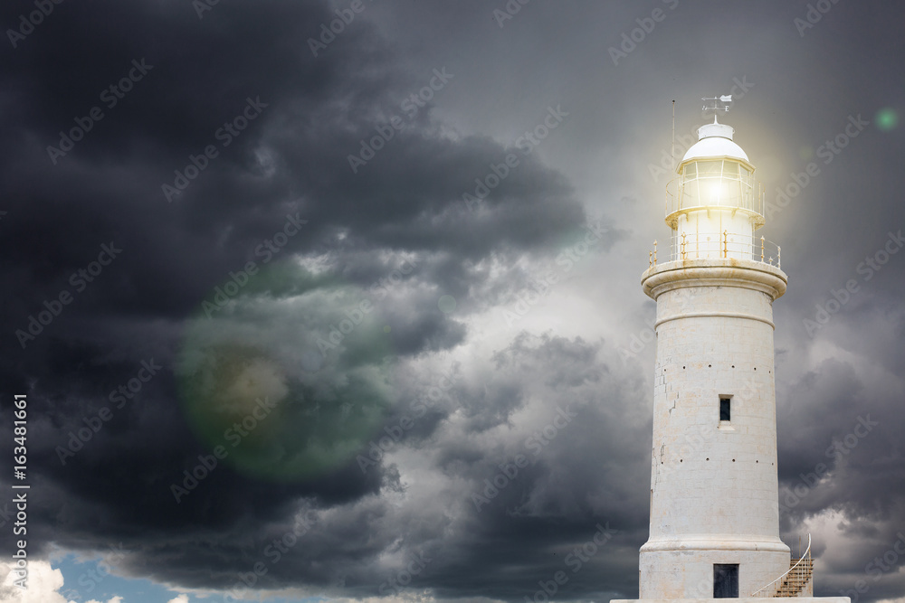 Lighthouse beaming light ray over stormy sky