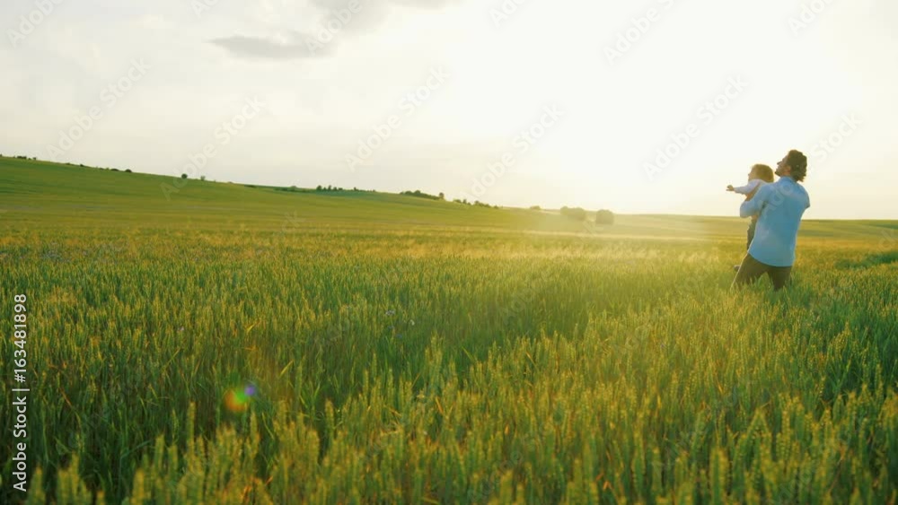 Happy family of man and little boy playing in green wheat field. Father raising his up towards the airplane. Close up Happy family of man and little boy playing in green wheat field. Father raising his up towards the airplane. Close up