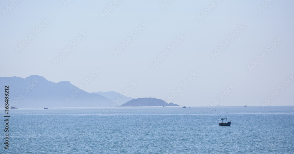 A beautiful seascape, a sailboat floating in the distance amidst majestic mountains.