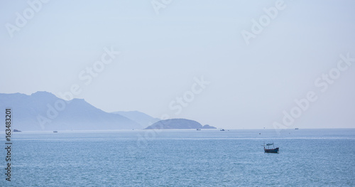 A beautiful seascape, a sailboat floating in the distance amidst majestic mountains.