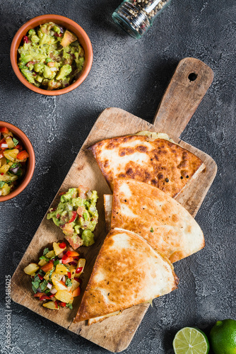 Grilled quesadillas (tortillas) with salsa, guacamole. Dark background, top view.