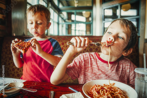 kids eat pizza and pasta at cafe. children eating unhealthy food indoors