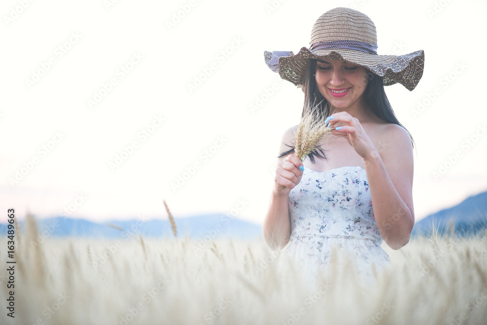 beautiful woman with summer hat in wheat field at sunset