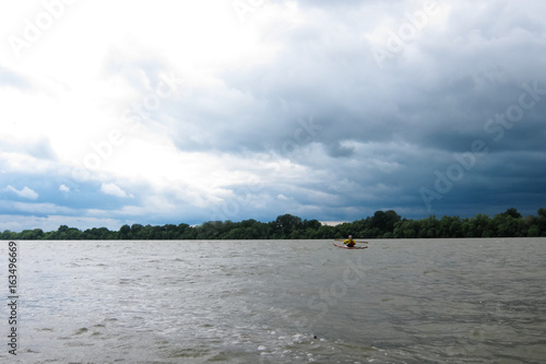 Man in selfmade wooden kayak in Danube river against background of storm sky. Kayaking in nature reserve of Danube Delta photo