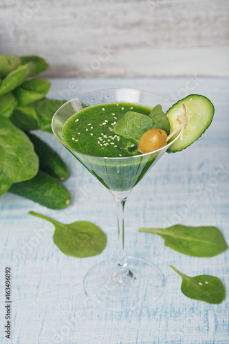 Green spinach and cucumber smoothie on light blue wooden background.