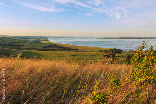 Scenic sea view from top of hills. Beautiful summer background. Amazing landscape with yellow meadows, green trees, blue sky, steep cliffs and picturesque bay. Panoramic photo. Camping, rest, relax.