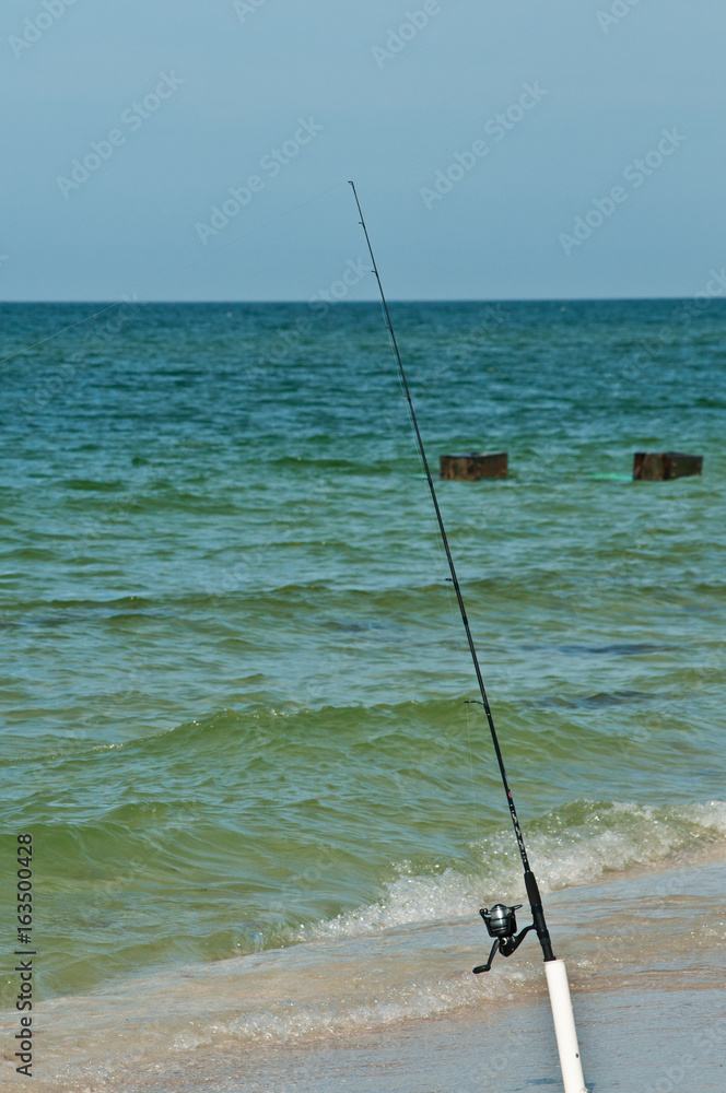 Single surf fishing pole in a pole holder on a tropical beach with line in  water of the tropical Gulf of Mexico on a sunny day Stock Photo