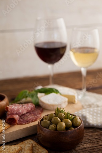 Green olives in container with ingredients and wineglasses