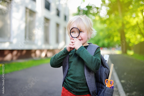 Cute little schoolboy with magnifying glass outdoors on sunny day. Back to school concept.