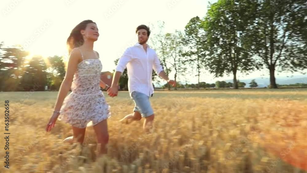 A young couple running across a wheat field / A man and woman in love in the middle of nature holding hands smiling and running in sunset light hand to hand / slow-mo / steady-cam A young couple running across a wheat field / A man and woman in love in the middle of nature holding hands smiling and running in sunset light hand to hand / slow-mo / steady-cam