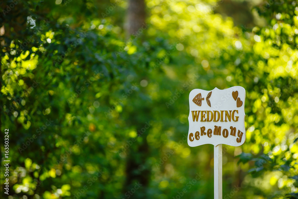 Wooden sign pointing to the wedding ceremony in the forest. Background green forest. Warm sunny day