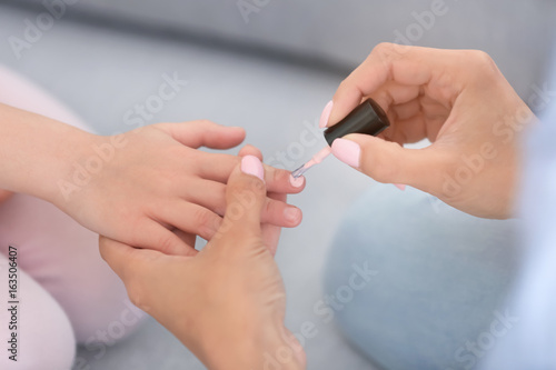 Young woman doing nails of her little daughter at home  closeup