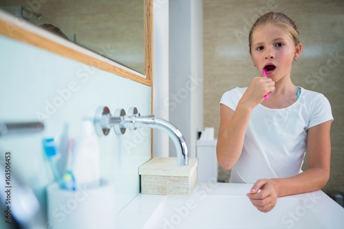 Portrait of girl brushing teeth in bathroom