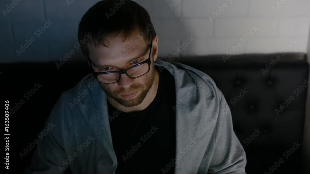 Young man in hood play video game sitting behind big monitor. His eyes browse the monitor. Young man in hood play video game sitting behind big monitor. His eyes browse the monitor.