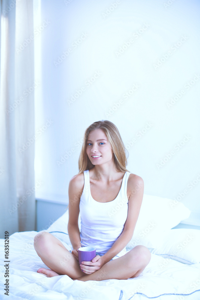 Pretty young woman reading the newspaper in bed and enjoying a cup of tea Pretty young woman reading the newspaper in bed and enjoying a cup of tea