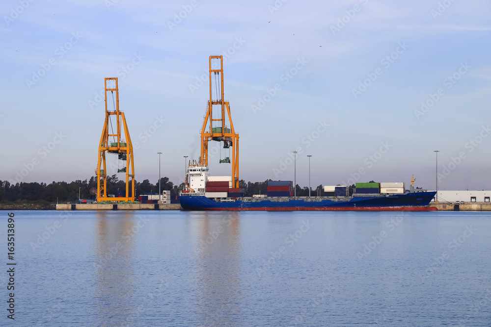 Obraz premium Cargo ship loading. Logistics and transportation with working crane bridge in harbor, logistic import export background and transport industry, Freight Transportation, Shipping, Nautical Vessel