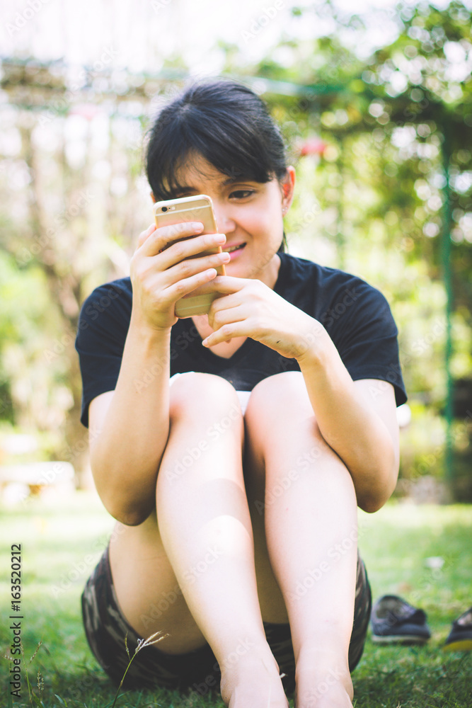 Happy young Asian woman with smartphone on a grass floor, Young female is reading information on web page via her mobile phone, Woman typing text message on smart phone Happy young Asian woman with smartphone on a grass floor, Young female is reading information on web page via her mobile phone, Woman typing text message on smart phone