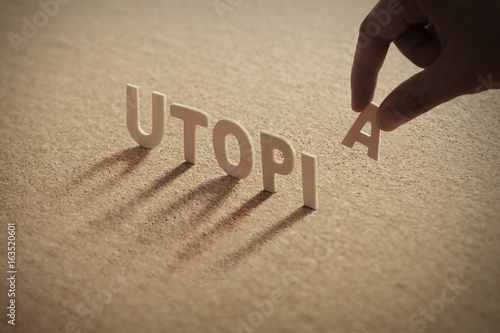 Photography UTOPIA wood word on compressed or corkboard with human's finger at A letter