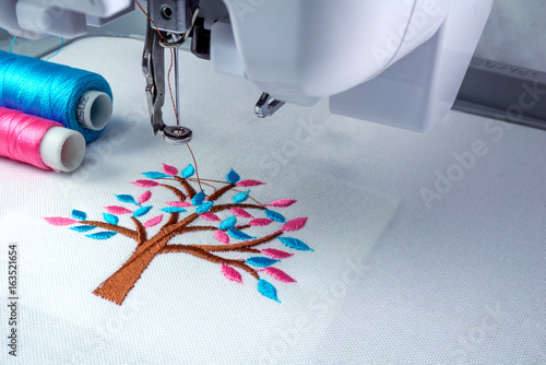 Close up picture workspace of  embroidery machine show embroider tree design theme. And two thraed s cyan and pink color. photo