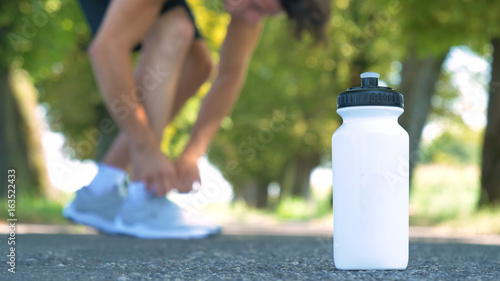 A sports white bottle (shaker) for drinking stands on the asphalt, the background runs through a man on the street. Concept: love sports, healthy lifestyle, be beautiful, muscles, happy, burn calories