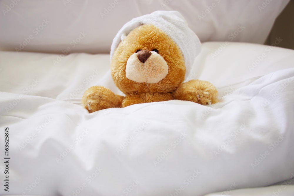 Lonely bear wears white towel on her head is sleeping on white pillow