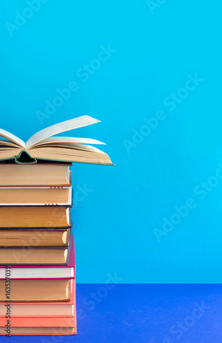 stack of textbooks with an open book on a blue background
