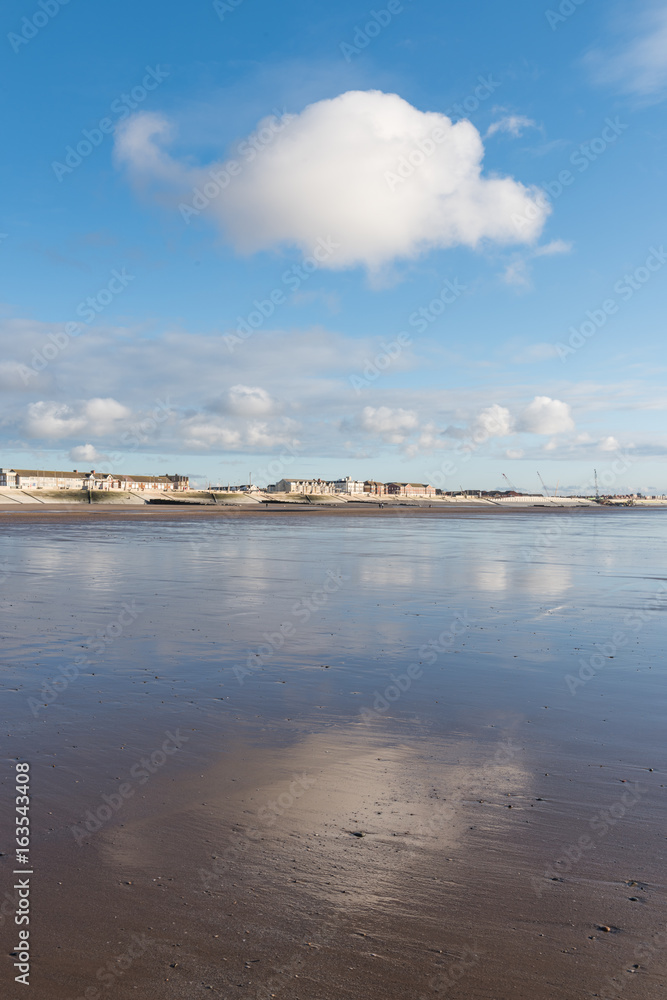 Beautiful blue sky and textured sand, on a cool sunny winters day at the beach. The clouds reflect off the wet sand.