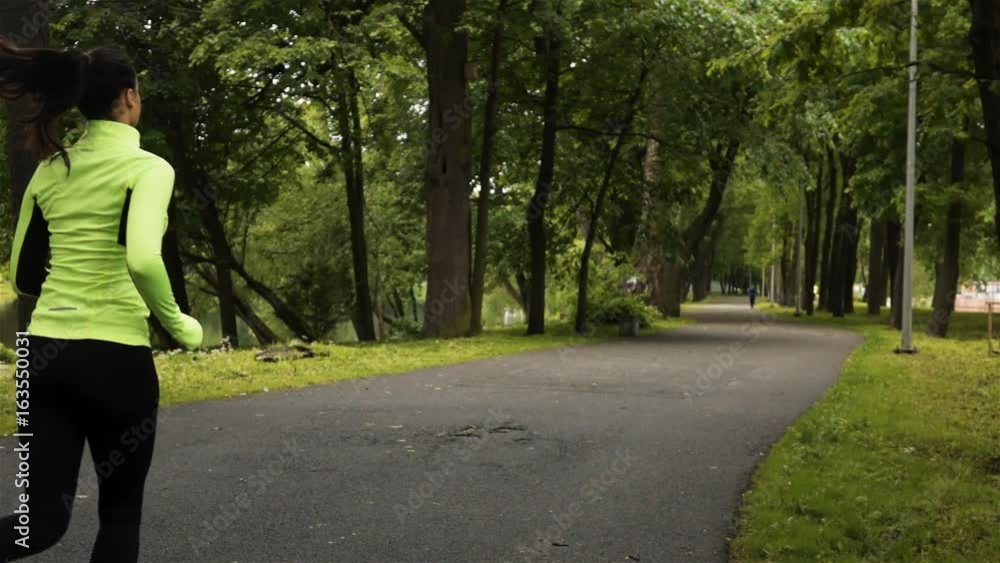 Runner woman running in park exercising outdoors. Steadicam stabilized shot. Wide back footage slow motion. Runner woman running in park exercising outdoors. Steadicam stabilized shot. Wide back footage slow motion.