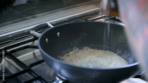 Unconventional chef is stiring and preparing base for sauce inside big pan, melts butter, adds sea salt chunks, grounded black pepper and other spices photo