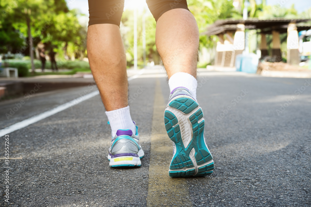 Runner athlete feet running on road. young man in sports clothing running in park