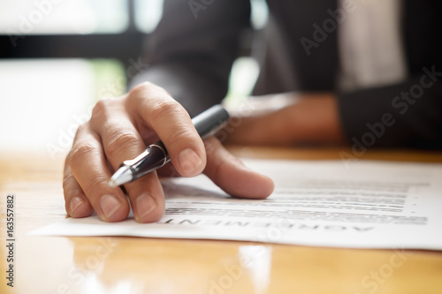 Hand of businessman in suit filling and signing contract,have a contract in place to protect it,signing of partnership agreement form clipped to pad closeup in office.