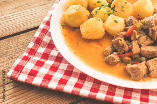 Goulash with meat, vegetables and potatoes on wooden table.