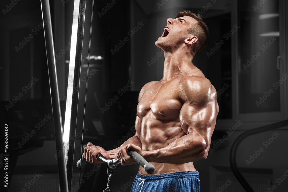 Muscular man working out in gym doing exercises at biceps, strong male naked torso abs Muscular man working out in gym doing exercises at biceps, strong male naked torso abs
