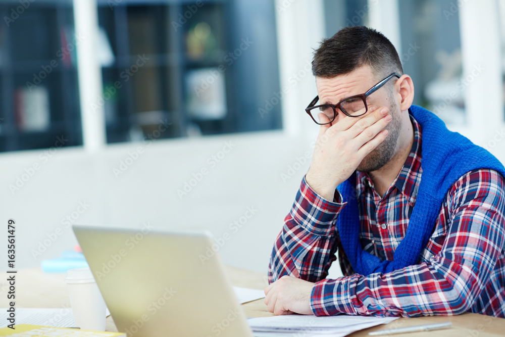 Tired designer or office manager sitting in front of laptop Tired designer or office manager sitting in front of laptop