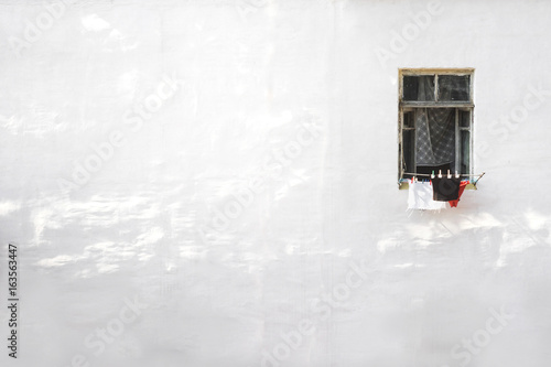 Small Window in an old house against a white textured wall at noon.