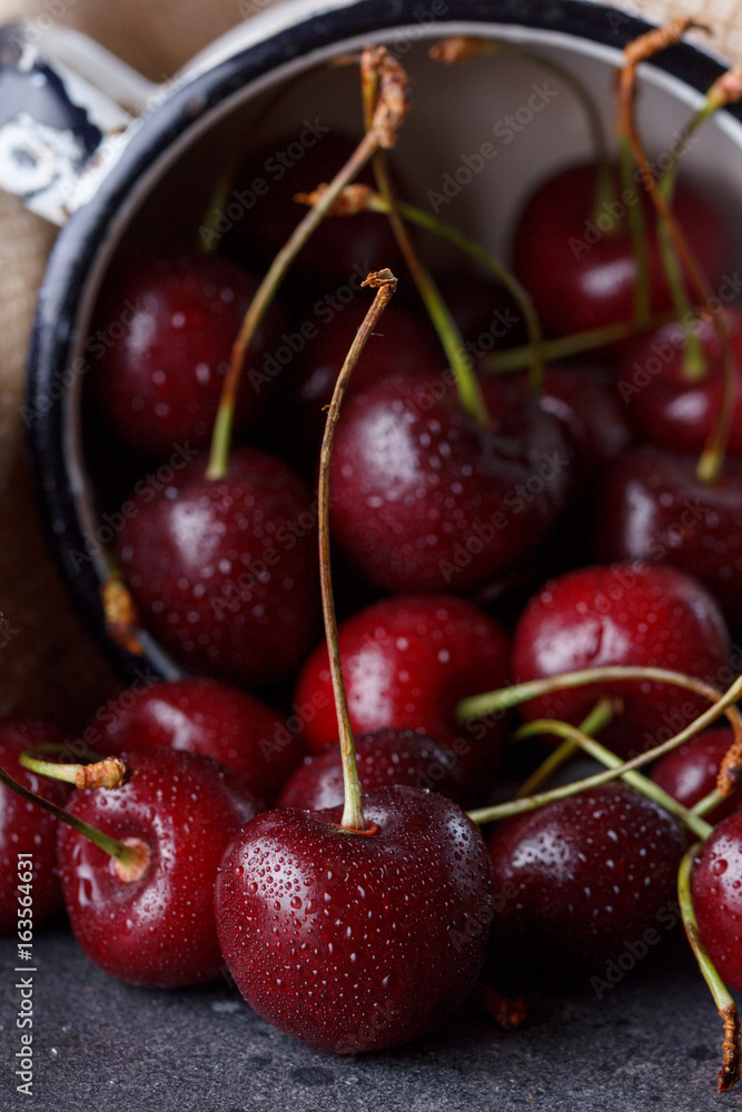 Red cherry in an enameled mug on a background of textile sackcloth. Red cherry in an enameled mug on a background of textile sackcloth.