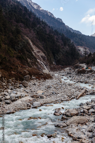 Black mountain with snow on the top. On the ground is frozen river with white stone and ice at Thangu and Chopta valley in winter in Lachen. North Sikkim, India. photo