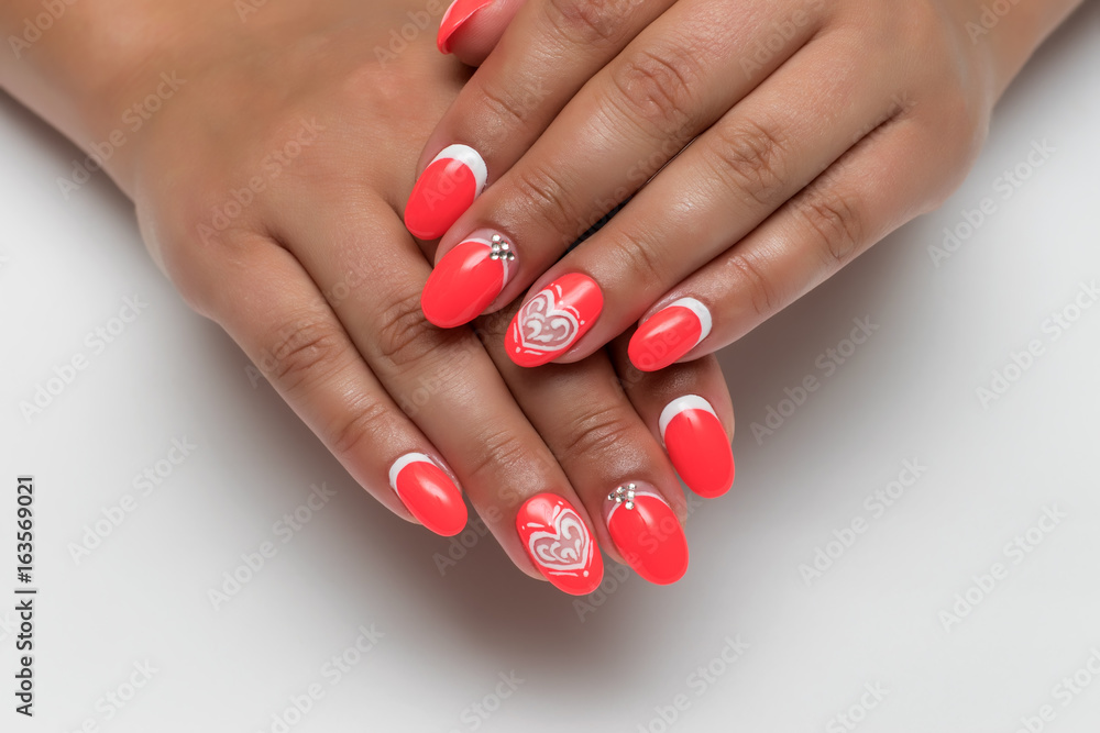 Year-old red-white manicure with a white heart and crystals on long oval nails on tanned hands Year-old red-white manicure with a white heart and crystals on long oval nails on tanned hands