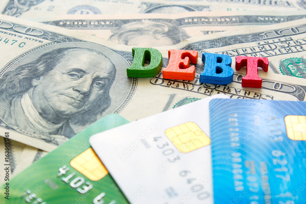 Fototapeta premium Word DEBT on a pile of money of dollar bills and bank credit cards