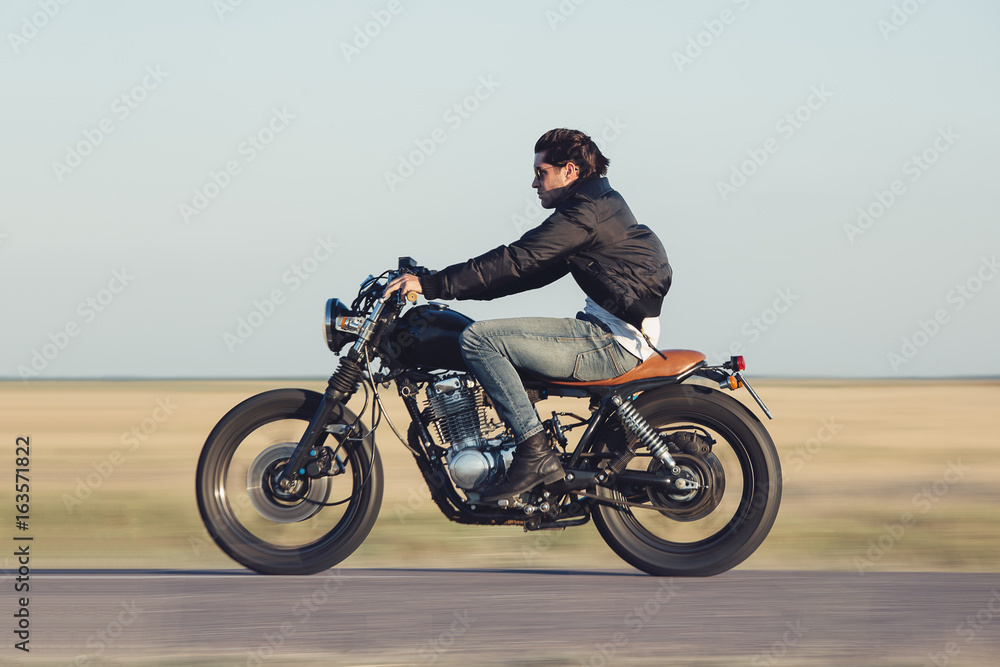 Fototapeta premium Młody człowiek na motocyklu vintage. Panoramowanie aparatu w celu uzyskania rozmycia ruchu.