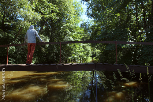 Man on wooden bridge over the river with lush green foliage. The river Jiesia in Lithuania, East Europe.