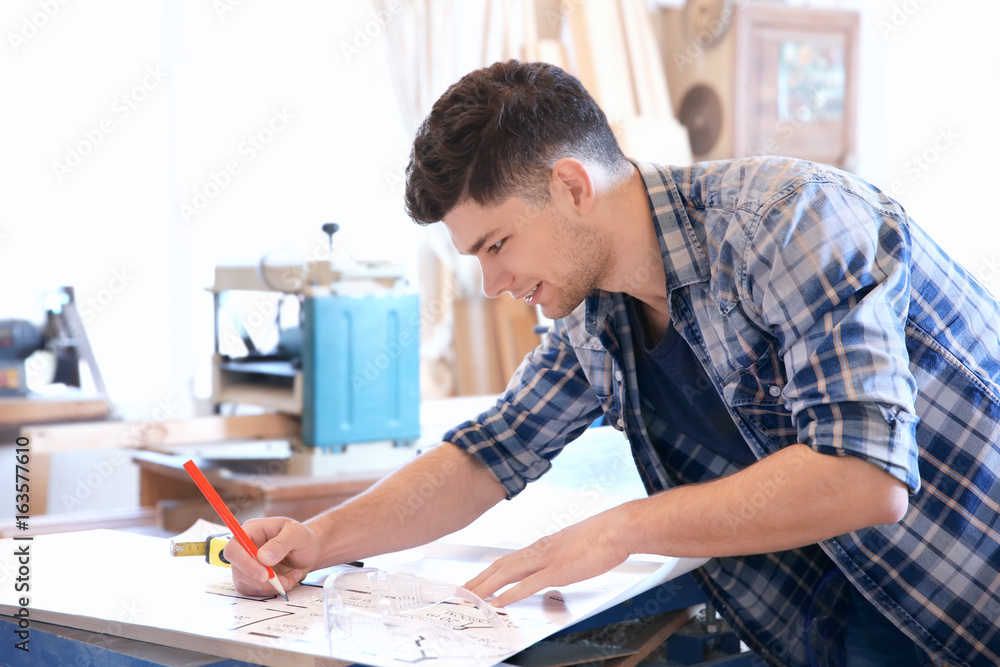 Handsome young carpenter checking drawing at table in workshop Handsome young carpenter checking drawing at table in workshop