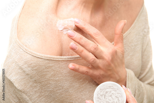Beautiful elderly woman applying body cream onto skin, on white background, closeup