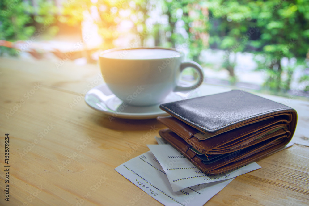 Soft tone of Money and credit card in a leather wallet with blur of hot coffee on wooden table and bill slip with natural background Soft tone of Money and credit card in a leather wallet with blur of hot coffee on wooden table and bill slip with natural background