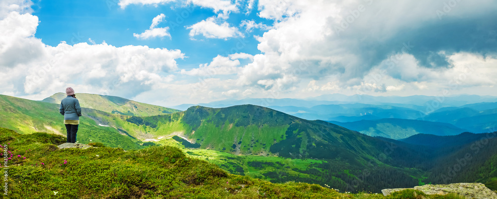 Naklejka premium woman tourist stands on top of a mountain and enjoys a panorama of mountain ridges and clouds