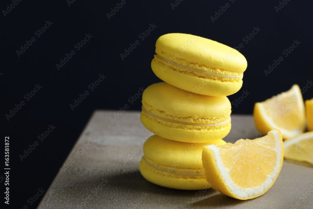 Tasty lemon macarons on table against dark background, closeup