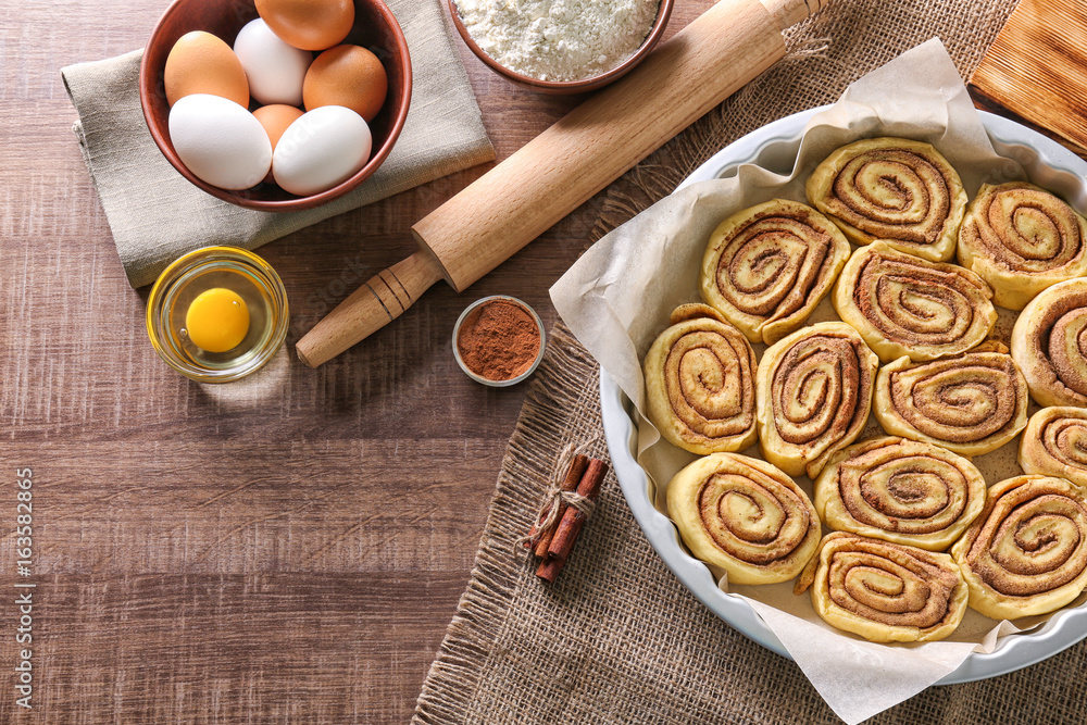 Raw cinnamon rolls in baking pan and ingredients on kitchen table Raw cinnamon rolls in baking pan and ingredients on kitchen table