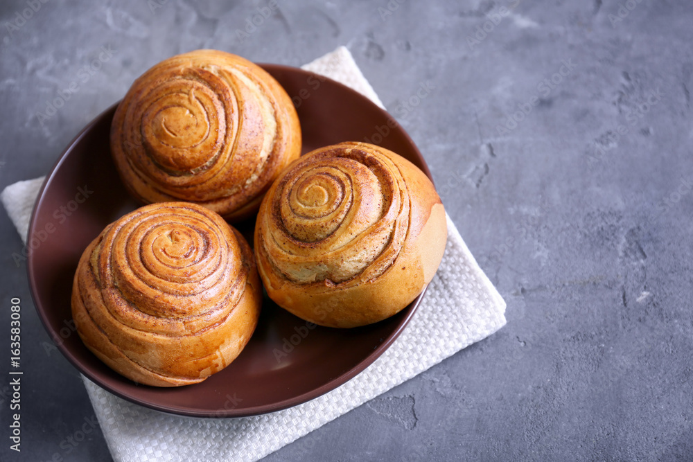Fototapeta premium Brown round plate with yummy cinnamon rolls on kitchen table