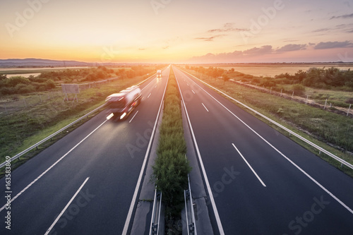 Highway landscape in a strong back light at sunset with motion blurred truck