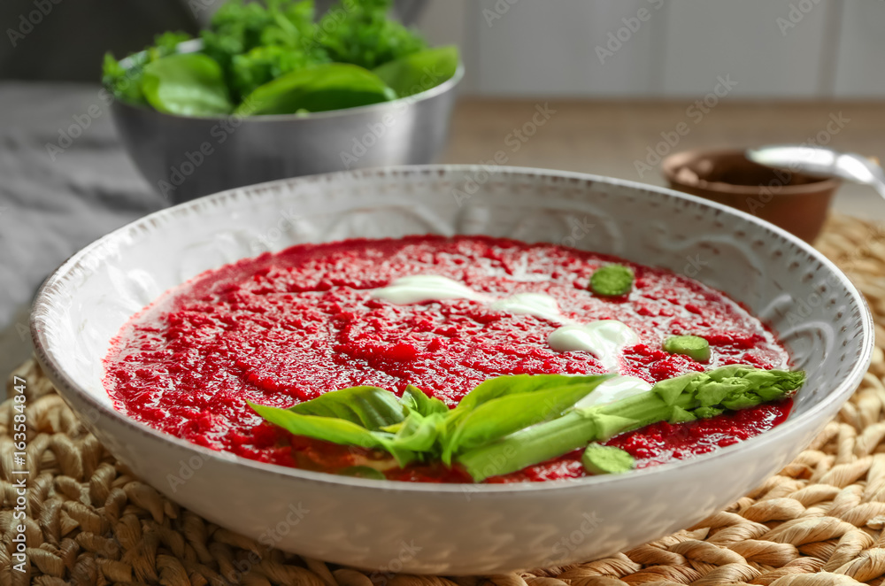 Delicious beet soup with basil leaves and asparagus on kitchen table